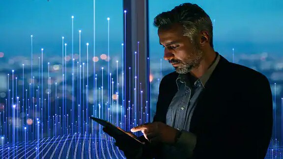 A man with a blazer using tablet near window of a building